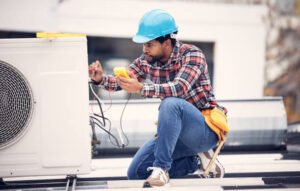 A man in a hard hat and blue shirt repairs an air conditioner, focused on fixing AC problems.