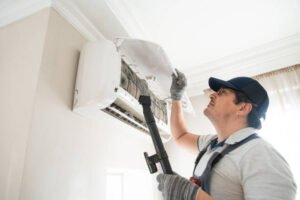 AC not turning on – technician in hat and overalls repairing an air conditioner in a well-lit setting.