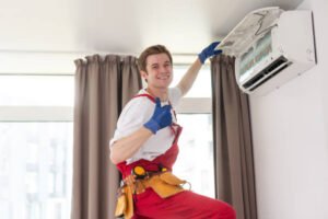 A man in overalls and safety gear repairs an air conditioner, focused on his task in a well-lit environment.