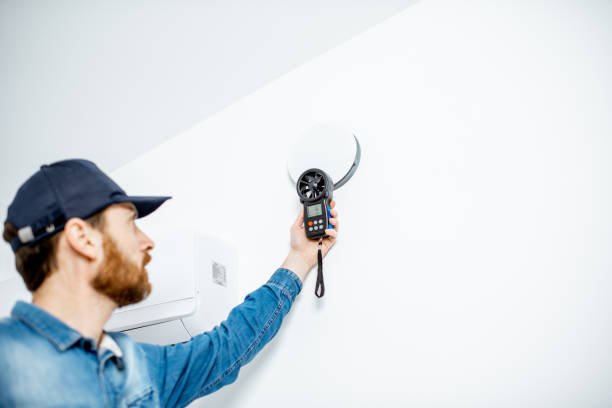 A man holds a remote control aimed at a wall, possibly adjusting a device or screen mounted on it to improve indoor air quality.