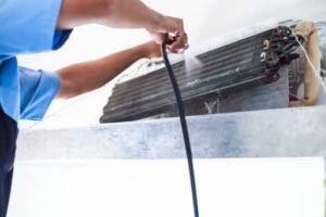 A technician performs annual AC maintenance by cleaning an air conditioner to improve efficiency and indoor air quality