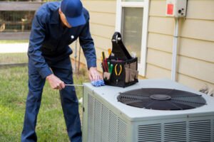 A man in blue overalls focused on Carrier 3-ton AC unit installation in a well-lit residential setting. 