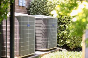 Two air conditioning units are positioned in front of a residential house, providing cooling for the home.