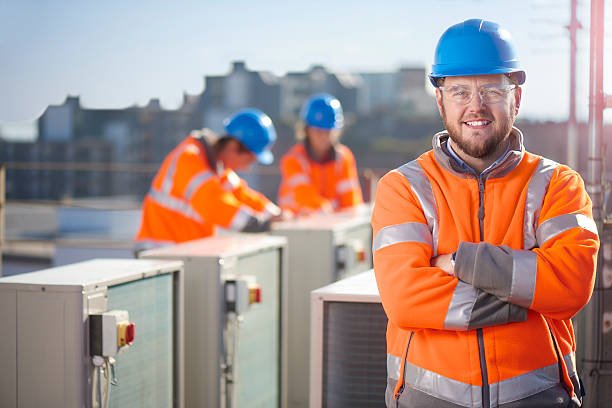 HVAC professional in an orange vest and hard hat stands in front of air conditioning units outdoors, helping homeowners choose the right HVAC system for their South Florida home