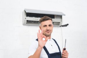 A technician in overalls smiles confidently and gives an 'OK' sign after completing same-day AC service in Broward County.