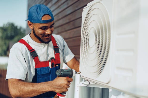 A man in blue overalls repairs an air conditioner, providing same-day AC service in Broward County.