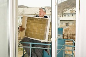 A man is holding a window air conditioner, preparing to install it in a home setting