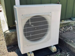 A small ac compressor placed on a wooden stand outdoors.