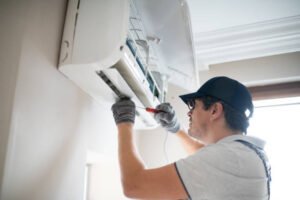 A man is fixing a wall AC unit, concentrating on the maintenance of the air conditioning system.