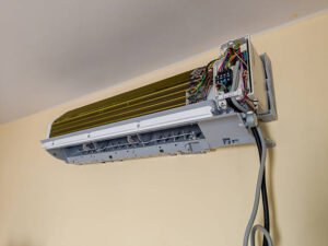 A man performing air conditioner repair by cleaning it with a green brush.