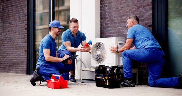 Three men in blue shirts repairing an air conditioner for an AC repair service.