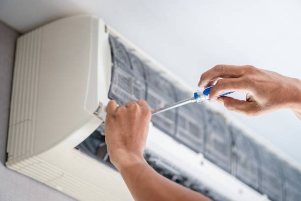 A technician repairs an air conditioner unit, focusing on its internal components with tools in hand.
