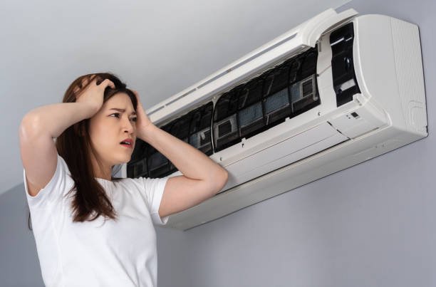 A woman examines her air conditioner, consideringWarning Signs to Replace Your Air Conditioner.