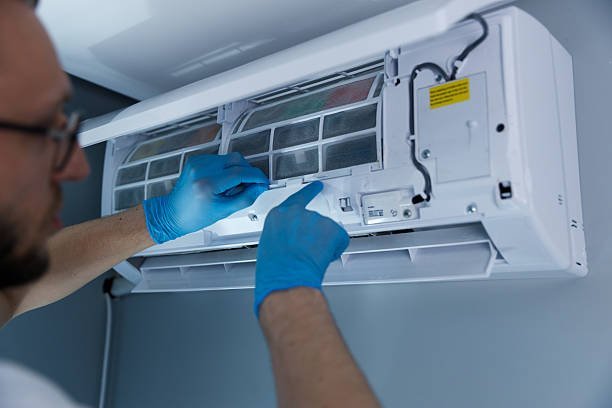 A man wearing blue gloves is repairing an air conditioner, demonstrating AC repair services.
