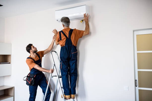 Two men installing a wall-mounted air conditioner, focused on the unit and tools in a residential setting.
