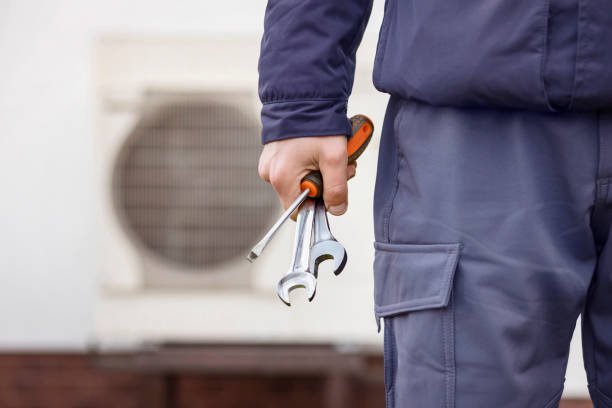 A technician holds a wrench and tool near an air conditioner, illustrating an AC repair service scenario.