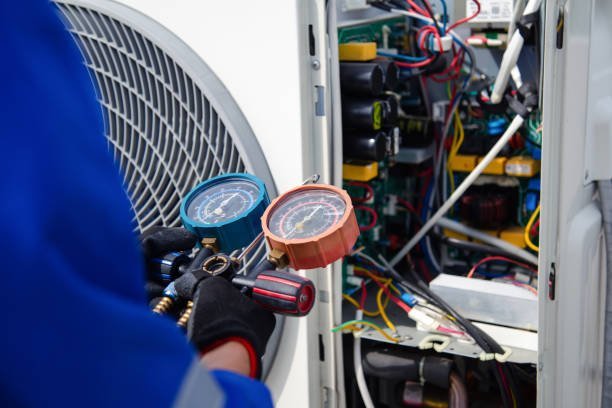 A person in blue overalls checks a gauge on an air conditioner during HVAC maintenance.