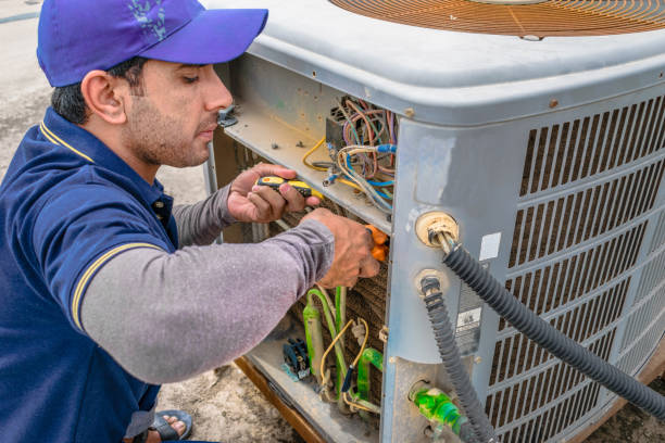 Two men wearing hard hats and vests are pointing at an ac installation.