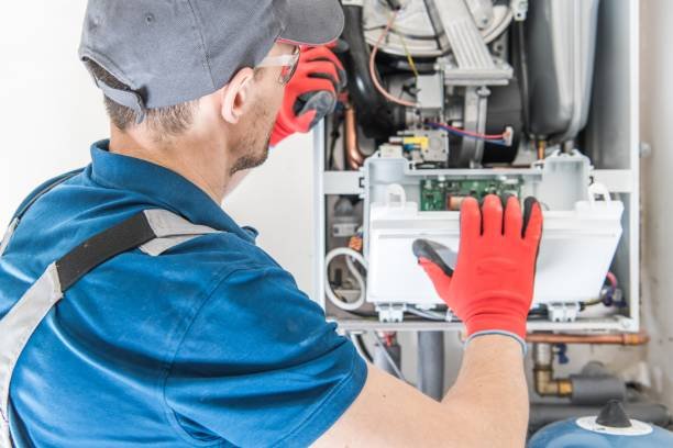 A man in a blue shirt and red gloves repairs a gas furnace during a residential HVAC service.