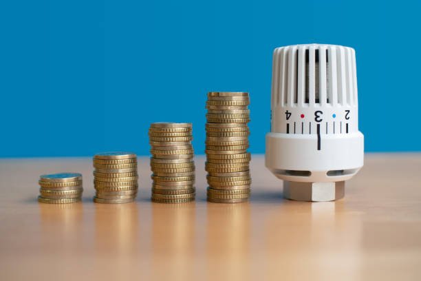 A thermometer next to stacks of coins on a table, symbolizing HVAC service costs and temperature regulation.