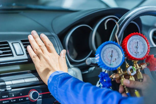 A person holds a gauge on a car's steering wheel, indicating work related to AC installation.