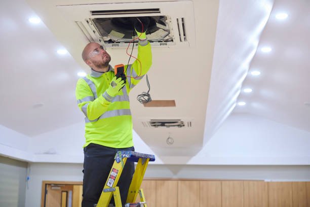 A man repairs a ceiling fan in a room, showcasing HVAC services in action.