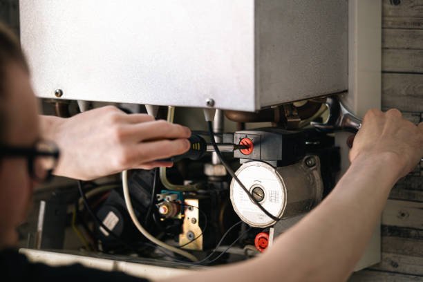 A man repairs a gas boiler as part of an HVAC replacement project in a residential setting.