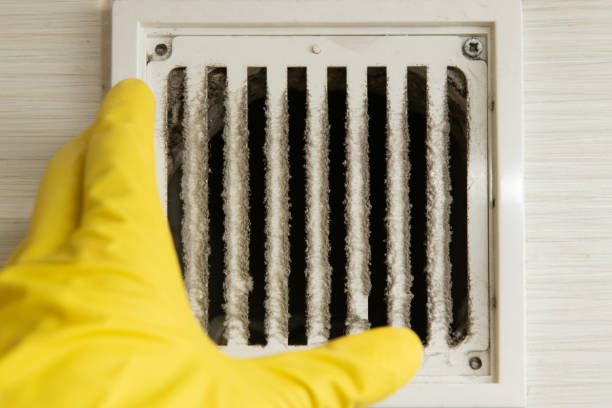 A person in yellow gloves holds a vent against a white wall, representing HVAC services in action.