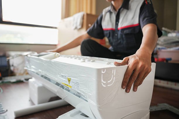 A man repairs a white air conditioner, focused on his task in an AC repair service setting.