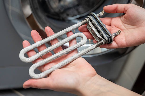 A person holds a metal heating element in front of a washing machine during an HVAC replacement process.