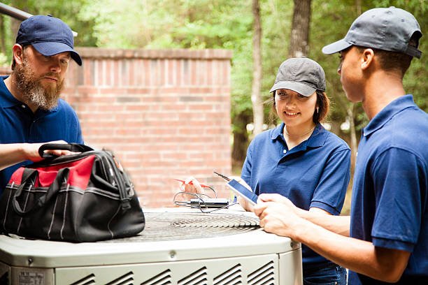 Three men and a woman discussing an air conditioner, representing HVAC services in a professional setting.
