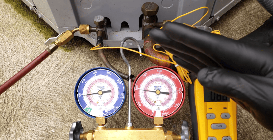 An individual wearing gloves checks a thermometer, assessing HVAC system performance.