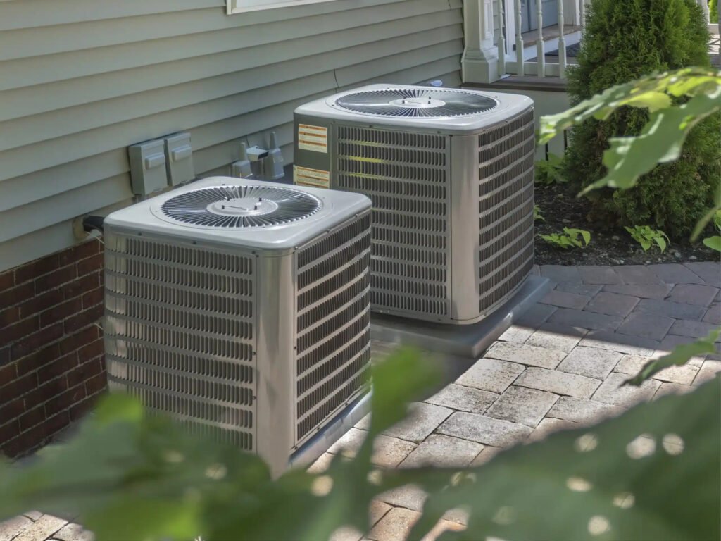Two air conditioning units placed on a brick patio, part of an HVAC system setup for outdoor cooling.