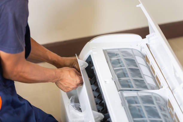 A man repairs an air conditioner that is blowing warm air, focused on fixing the internal components.