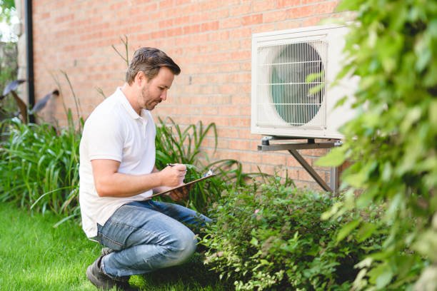 A man kneels in front of an air conditioner, which is blowing warm air into the room.