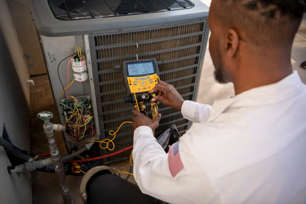 A man in a white shirt and pants checks an air conditioner's temperature with a digital thermometer during an emergency repair.