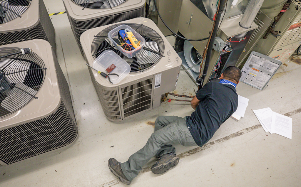 A technician works on an HVAC system in a spacious warehouse, focusing on maintenance tasks.