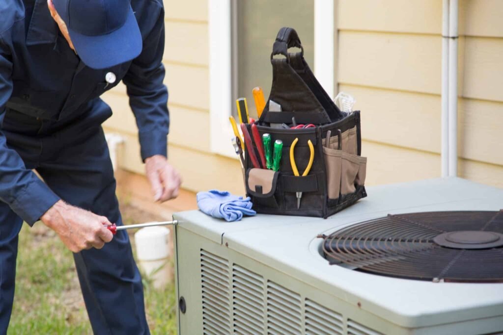 A man in a blue uniform repairs an air conditioner, representing HVAC contractors at work.